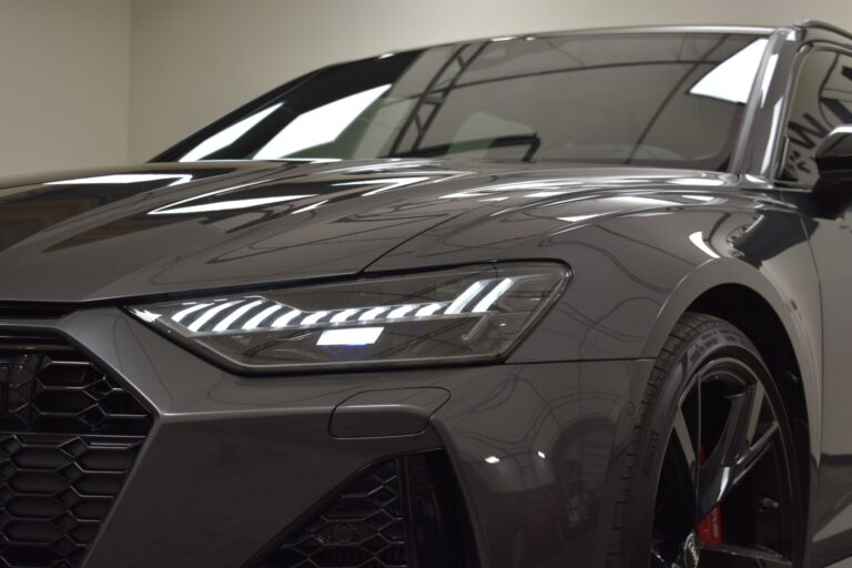 Close-up of the front left side of a dark grey car, highlighting its LED headlights and part of the grille.