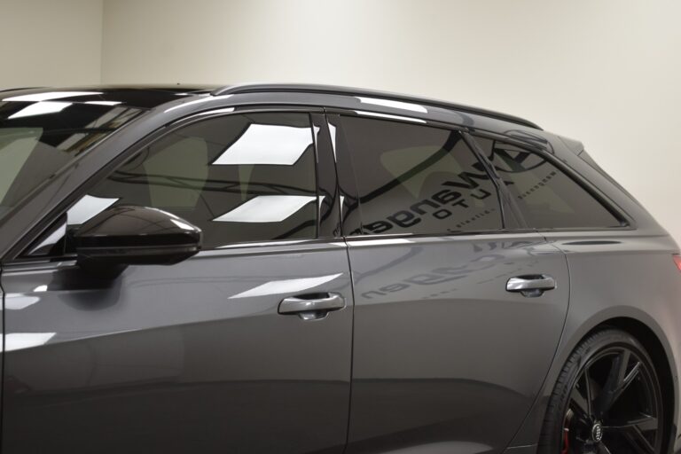 Close-up view of a grey car's tinted side windows and door handles in an indoor setting.