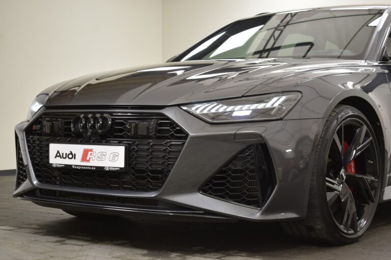 Close-up of the front of a gray Audi RS6 car showing its grille, headlights, and part of the bumper on a brick-paved surface.