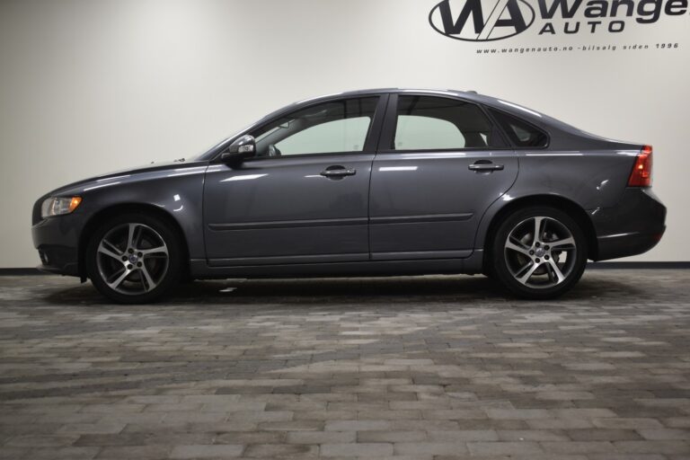 A gray sedan parked indoors on a tiled floor with the sign "MÅS Wange Auto" in the background.