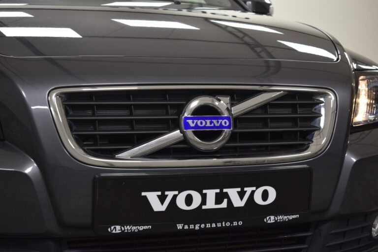 Close-up of a black Volvo car's front grille, featuring the Volvo logo and a license plate with the text "VOLVO" and additional text "Wangenauto.no".