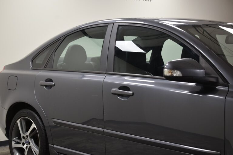 Side view of a parked dark gray sedan with closed windows and a visible side mirror, shown indoors under artificial lighting.