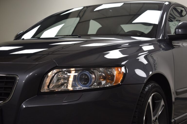 Close-up of the front right side of a dark-colored car showing the headlight, side mirror, and part of the windshield.