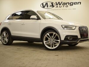 A white Audi SUV is parked indoors on a tiled floor. The background features the logo and website of Wangen Auto. The vehicle's front and side are visible, showcasing its design and large wheels.