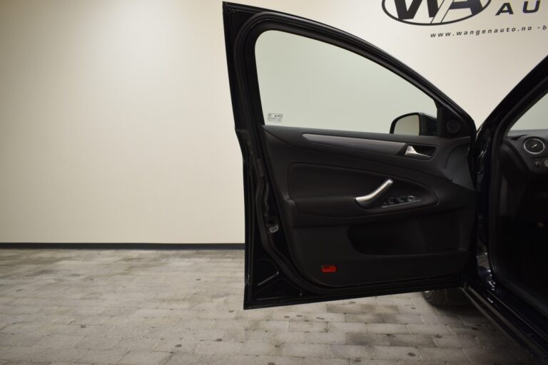 An open front driver's side door of a black car, showcasing the interior panel and door controls. The car is parked on a concrete floor next to a beige wall.